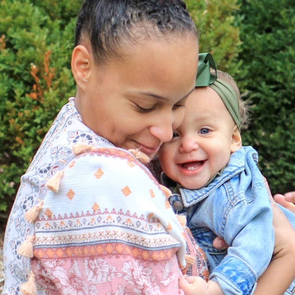 A woman holding a baby in front of bushes.